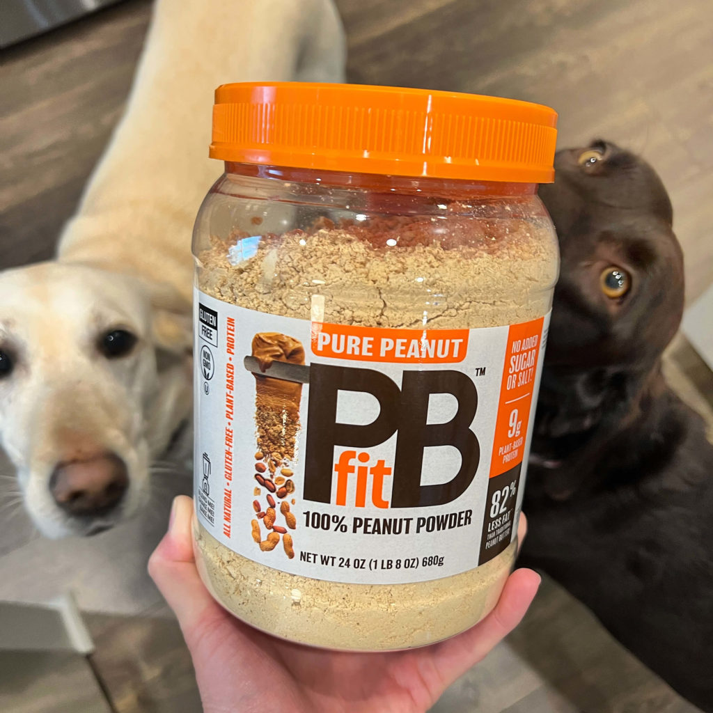 Two Labradors check out their container of PBfit Pure Peanut