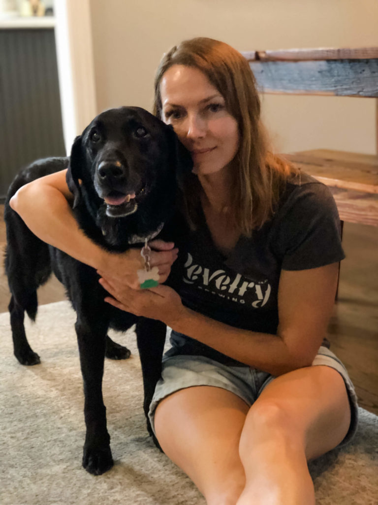 Woman sits on the floor with her arm around a senior Black Labrador