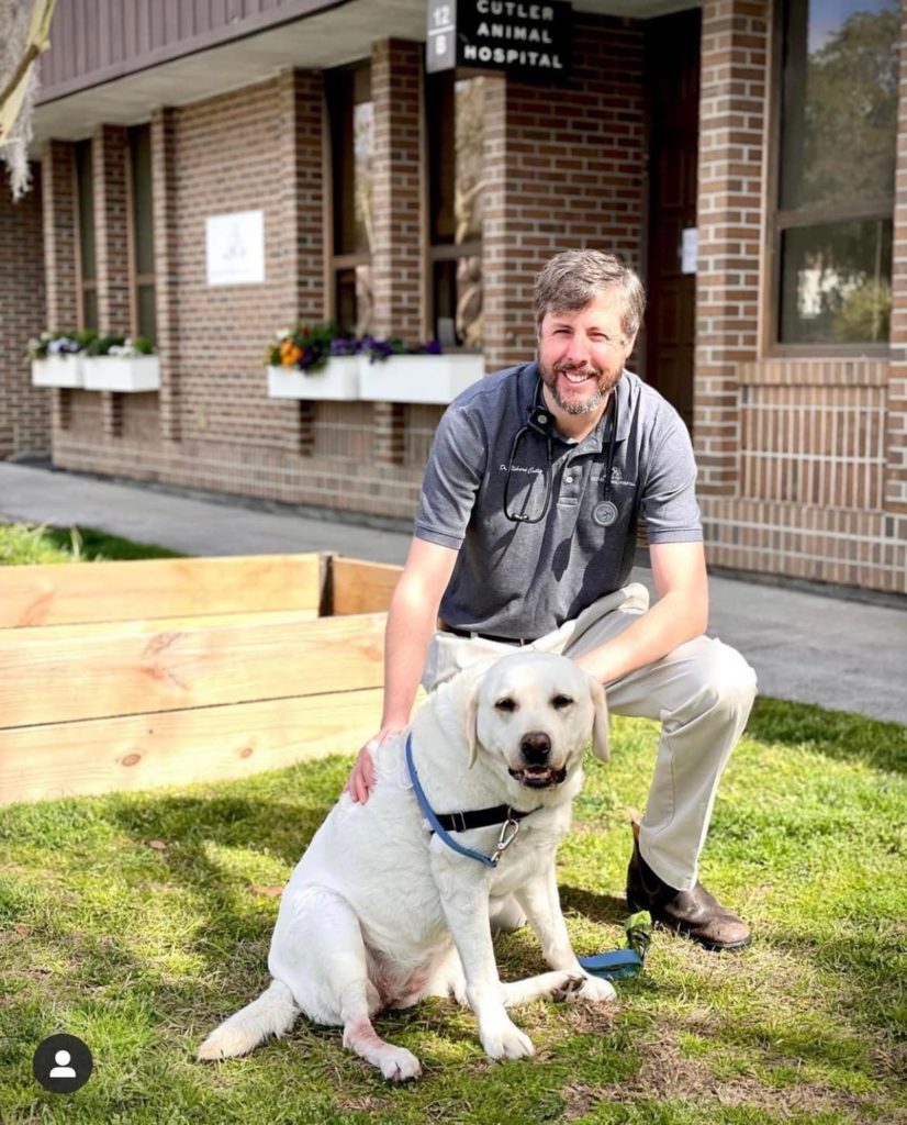 Veterinarian Richard Cutler kneels with a yellow Labrador in front of his Charleston, SC veterinary clinic.